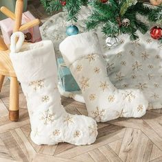 two white christmas boots sitting on top of a wooden floor next to a christmas tree