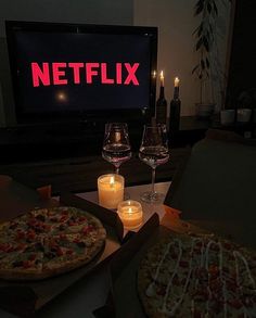 two pizzas sitting in front of a tv with candles on the table next to them