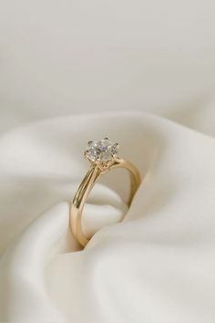 an engagement ring on top of a white satin material with a diamond in the center