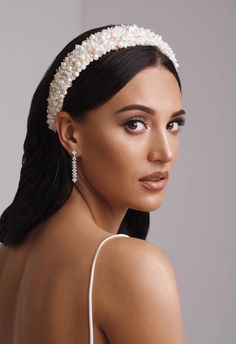 a woman wearing a white headband with pearls on it's side and her hair pulled back