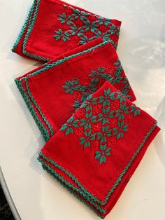 two red napkins with green leaves on them sitting on a table next to each other