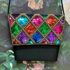 "Vintage 80's shoulder purse has bright rainbow sequins edged with gold beads in a harlequin pattern on the front flap. The body of the purse is black satin. It has a braided shoulder cord and magnetic snap front closure. The cord folds in to convert to a clutch. Interior is black satin with one pocket. Clean condition inside and out with a light mark on the back. Purse measures 7.5\" at its widest by 6.5\". Please see photos for more details. All items are vintage that are preowned. All of the Multicolor Sequined Evening Bag, Multicolor Sequined Shoulder Bag For Party, Evening Multicolor Sequins Bag, Multicolor Shoulder Bag For Party Festivals, Multicolor Shoulder Bag For Evening Festivals, Multicolor Evening Bags For Festivals, Multicolor Evening Shoulder Bag For Festivals, Evening Multicolor Shoulder Bag For Festivals, Formal Multicolor Embellished Shoulder Bag