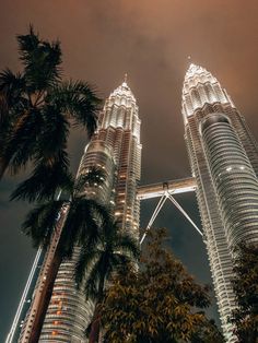 two very tall buildings towering into the sky at night with palm trees in foreground