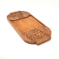 a carved wooden tray with grapes on the bottom and leaves at the top, against a white background