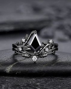 a black and white diamond ring sitting on top of a piece of stone with leaves