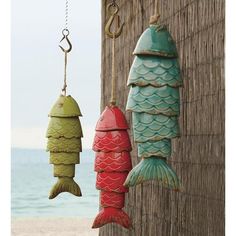 three fish hanging from hooks on the side of a wooden wall next to water and beach