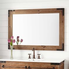 a bathroom vanity with a mirror above it and flowers in a vase on the counter