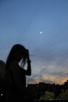 a woman is looking at the moon in the sky with her hand on her head