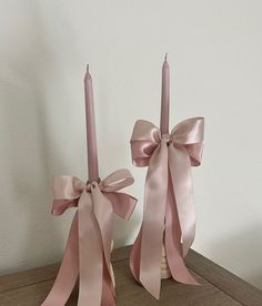 two pink candles with bows on them sitting on a table