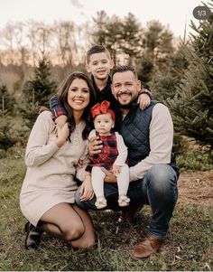 a man and woman pose for a family photo in front of a christmas tree farm