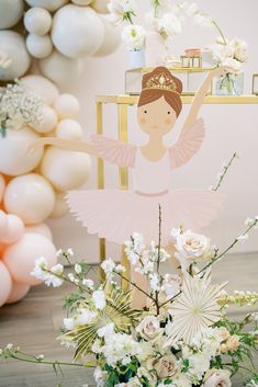 a ballerina doll sitting on top of a chair next to some flowers and balloons