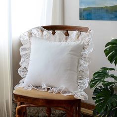 a white pillow sitting on top of a wooden chair next to a potted plant