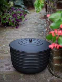 a large black pot sitting on top of a brick walkway next to a flower garden