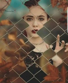 a woman behind a chain link fence with her hand up to the camera, making a weird face