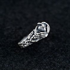 Dive into the darker side of symbolism with this sterling silver skeleton hand ring gripping a heart. This intricately designed ring captures the essence of love, loyalty, and mystery in a unique gothic style. With skeletal hands holding a heart, this ring is perfect for those who appreciate the beauty in the macabre. The detailed craftsmanship and dark aesthetic make it an ideal accessory for fans of alternative fashion and gothic jewelry. Handmade with attention to detail, this ring features a Hand Cast Silver Skull Promise Ring, Gothic Sterling Silver Promise Ring, Symbolic Sterling Silver Skull Ring, Sterling Silver Open Skull Ring, Symbolic Style, Symbolic Sterling Silver Open Skull Ring, Gothic Hand Cast Sterling Silver Skull Ring, Hand Cast Gothic Skull Ring In Sterling Silver, Gothic Culture, Halloween Ring