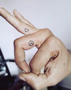 two fingers with peace signs and hearts tattooed on them