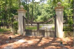 an iron gate with two pillars in the middle of a wooded area, surrounded by trees