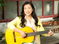 a woman sitting on a bench with a guitar in her hand and smiling at the camera