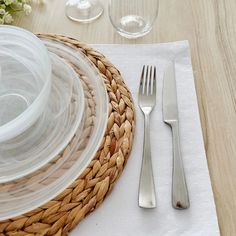 a place setting with silverware on a white table cloth and wicker basket next to it