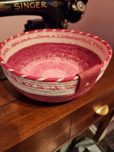 a pink and white bowl sitting on top of a wooden table next to a sewing machine