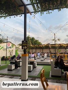 an outdoor seating area with string lights and people sitting at tables on the grass in front of it