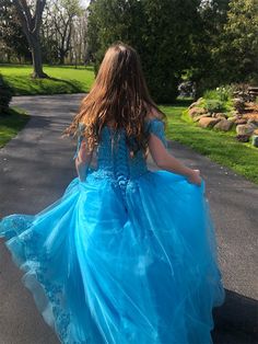 a girl in a blue dress walking down the street with her back to the camera