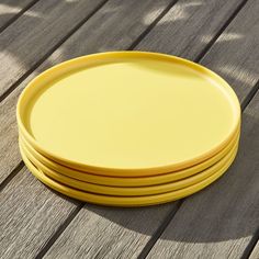 four yellow plates sitting on top of a wooden table next to each other in the sun