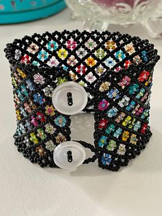 This cuff-style beaded bracelet is made of size 11/0 seed beads, opaque black with flowers in various colors.  Closure is 2 small buttons (clear) and bead loops.  Bracelet is 2" wide. Size: 6 3/4" (band is 6 1/2", clasp adds 1/2".) I recommend measuring your wrist and adding 1/2" for best fit. Seed Bead Bracelet, Bracelet Black, Seed Bead Bracelets, Bead Bracelet, Seed Bead, Beaded Bracelet, Seed Beads, Jewelry Bracelets, Seeds