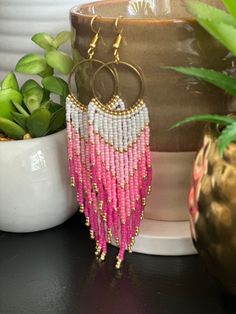 a pair of pink and white beaded earrings sitting next to a potted plant