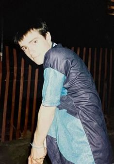 a man in blue shirt and jeans leaning on a wooden fence with his hand on the ground