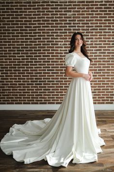 a woman standing in front of a brick wall wearing a wedding dress with short sleeves