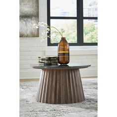 a vase sitting on top of a wooden table next to a book and glass bottle