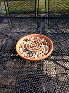 a bowl filled with rocks sitting on top of a metal grill grate next to a green field