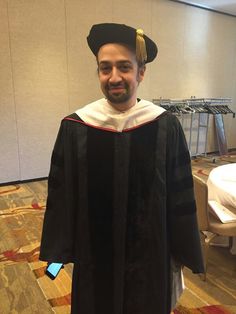 a man in a graduation gown and cap is posing for the camera with his cell phone