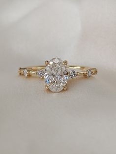 a close up of a diamond ring on a white cloth with gold band and side stones