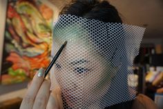 a woman holding a pencil in front of her face with a net covering it's head