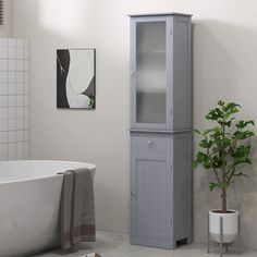 a white bath tub sitting next to a tall cabinet in a bathroom with a potted plant on the floor