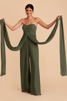 a woman in a strapless top and wide legged pants holds up a green scarf