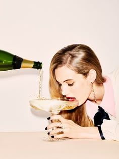 a woman sitting at a table with a wine glass in front of her and a bottle behind her