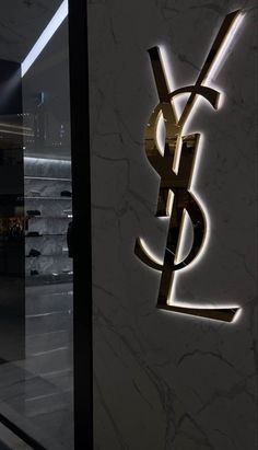 the ysl logo is lit up in front of a wall with marble walls and flooring