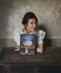 a woman sitting at a table with a book in front of her face and looking up