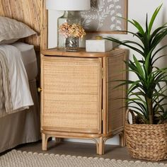 a wicker cabinet next to a bed with a plant in it and a lamp on top