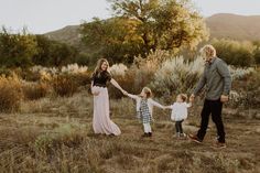 an adult and two children holding hands while walking through a field