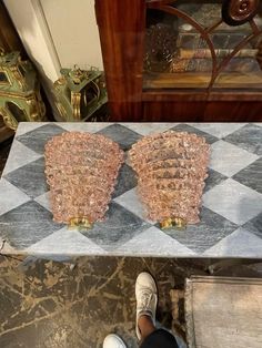 two pieces of glass sitting on top of a checkered tile floor next to a person's feet