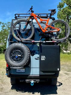 an orange bike is mounted to the back of a blue jeep with two bikes on top