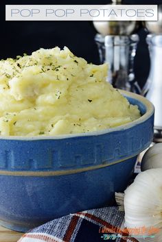 a blue bowl filled with mashed potatoes on top of a wooden table next to garlic