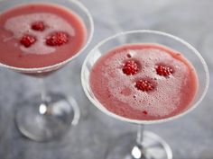 two martinis with raspberries in them on a gray table top, one is empty and the other half has watermelon