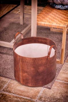 a brown leather basket sitting on top of a floor next to a wooden table and chair