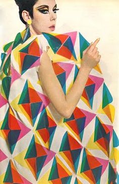 a woman in a colorful dress is holding her hand up to her chest and looking at the camera