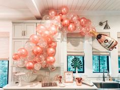 balloons and champagne are hanging from the ceiling above a kitchen counter with white cabinetry